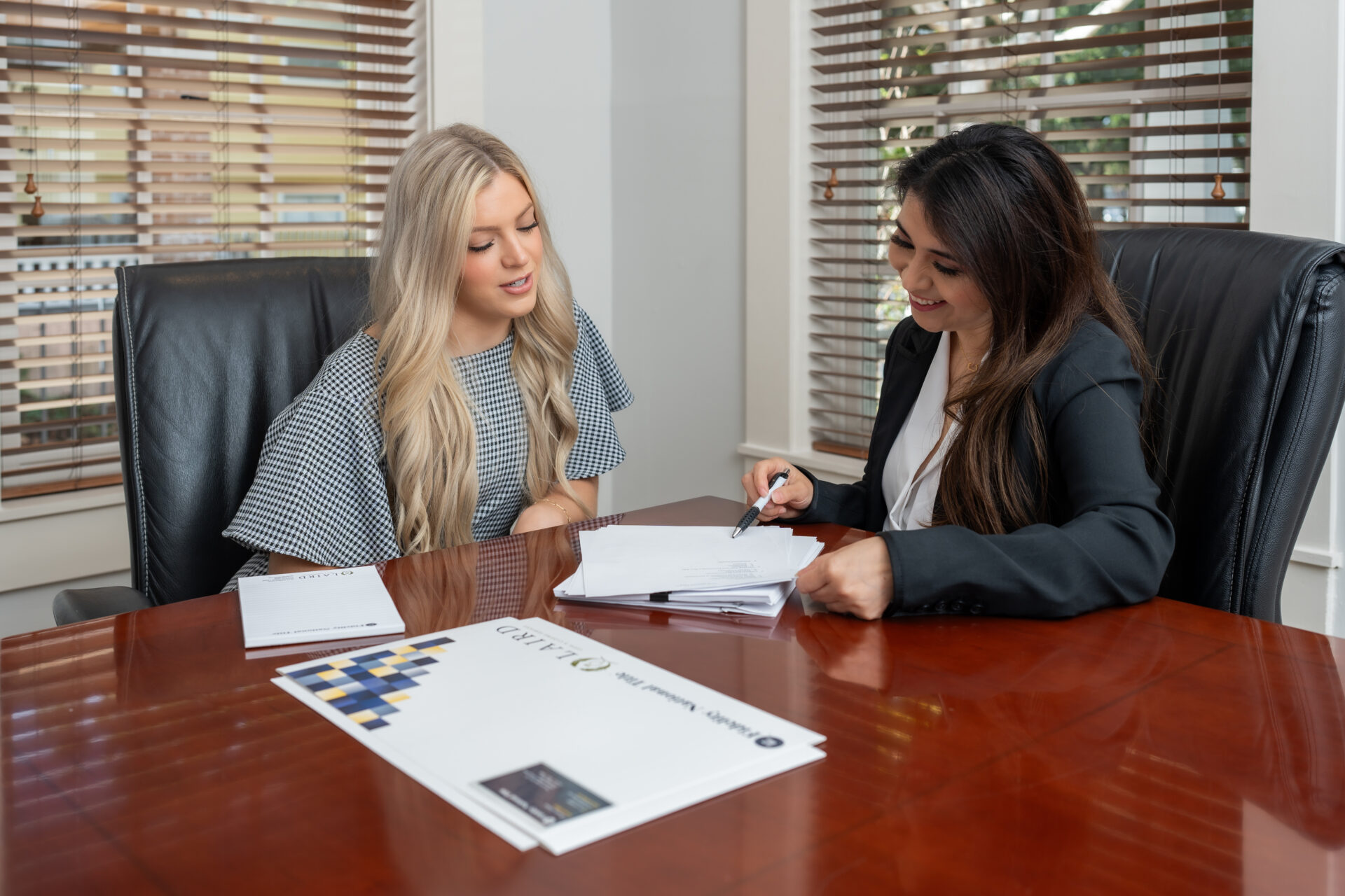 Two women sitting at a table with papers and pens.